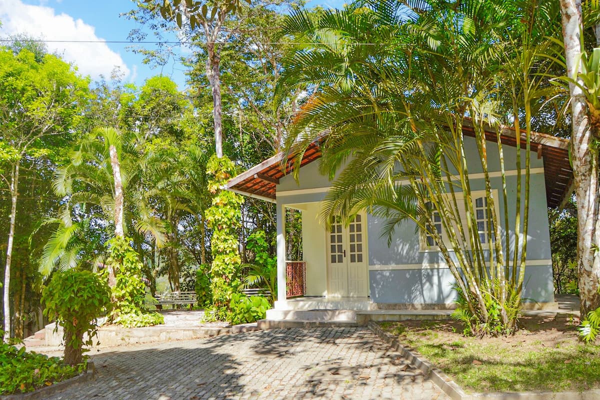 A house with a tiled porch, surrounded by lush greenery and trees.