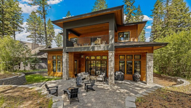 A modern two-story house with a balcony, stone exterior, and a patio with outdoor furniture. - Fox & the Fairway- On the golf course in Spring Mtn Ranch w/ AC & club access (McCall)