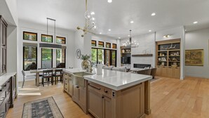 A spacious kitchen with a large island, wooden cabinets, and a built-in oven. There are multiple windows providing natural light and views of the outdoors. - Fox & the Fairway- On the golf course in Spring Mtn Ranch w/ AC & club access (McCall)