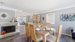A dining area with a fireplace, dining table set with plates, glasses, and a clock on the wall. - Cozy Heights Retreat | Baker's Kitchen & Sleeps 10 (Windsor Heights)