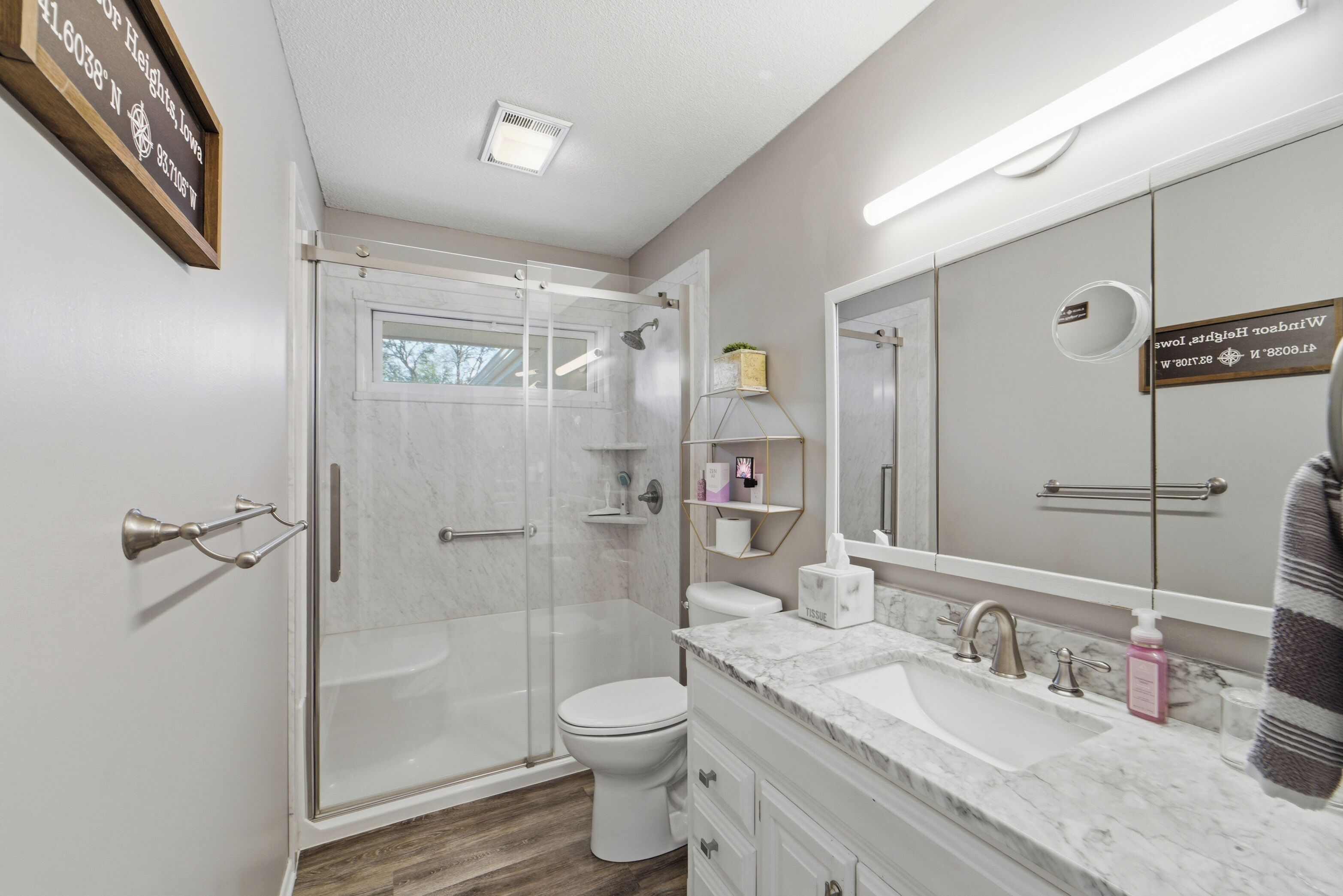 Une salle de bain moderne avec une douche à parois de verre, des toilettes blanches et un lavabo en marbre agrémenté d’un grand miroir.