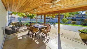A covered patio with a wooden ceiling, a table with chairs, and a view of a residential neighborhood. - Cozy Heights Retreat | Baker's Kitchen & Sleeps 10 (Windsor Heights)