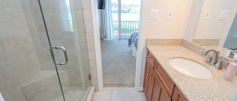 A bathroom with a glass shower enclosure, a sink with a granite countertop, and wooden cabinets.