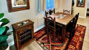 A dining area with a wooden table, chairs, a patterned rug, and a hanging light fixture.