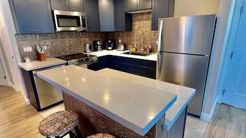 A modern kitchen with dark cabinets, a stainless steel refrigerator, and a central island with stools.