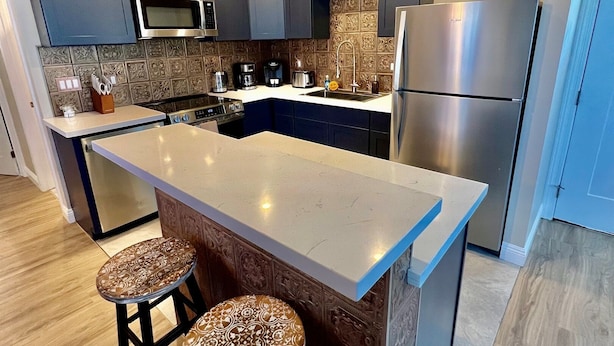 A modern kitchen with dark cabinets, a stainless steel refrigerator, and a central island with stools.