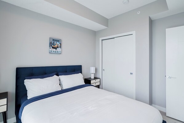 Una camera da letto moderna con un letto grande, un comodino con una lampada, un quadro appeso alla parete e una porta chiusa.