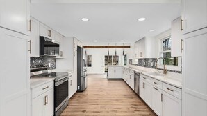 Une cuisine moderne avec des meubles blancs, des appareils en acier inoxydable et un plancher en bois.