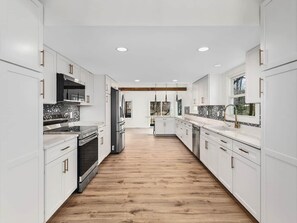 A modern kitchen with white cabinetry, stainless steel appliances, and a wooden floor. - 1mi to Downtown |Hot Tub - Fenced Yard - Game Room (Waynesville)