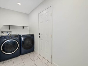 A laundry room with two front-loading washing machines, a white door, and a tiled floor. - 1mi to Downtown |Hot Tub - Fenced Yard - Game Room (Waynesville)