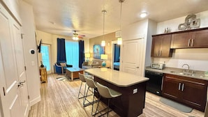 A modern kitchen with a central island, bar stools, and a dining area with a sofa and coffee table. - Spacious 2-Bedroom Urban Oasis (Salt Lake City)