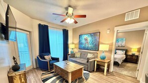 A well-lit living room with a ceiling fan, a sofa, a coffee table, and a TV. - Spacious 2-Bedroom Urban Oasis (Salt Lake City)