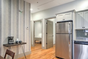 A modern kitchen with stainless steel appliances, a coffee station, and a hallway leading to a bedroom. - The Marquee at Heirloom Asheville | Historic Downtown Asheville Condo (Asheville)
