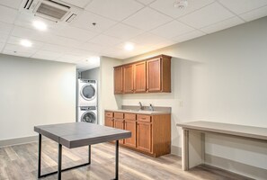 A kitchenette with wooden cabinets, a washing machine, and a table. - The Marquee at Heirloom Asheville | Historic Downtown Asheville Condo (Asheville)