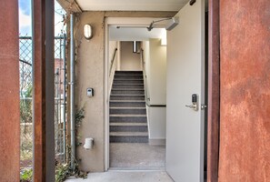 Un escalier étroit mène à une porte, avec une grille en métal et quelques plantes sur le côté gauche.