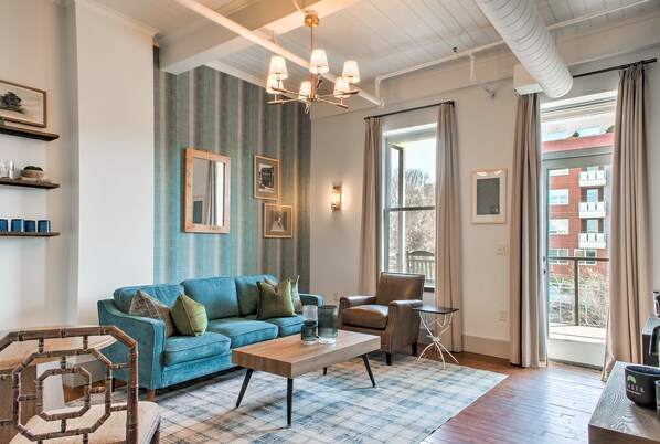 A living room with a blue sofa, a wooden coffee table, a brown leather chair, and a view of a building through a large window.