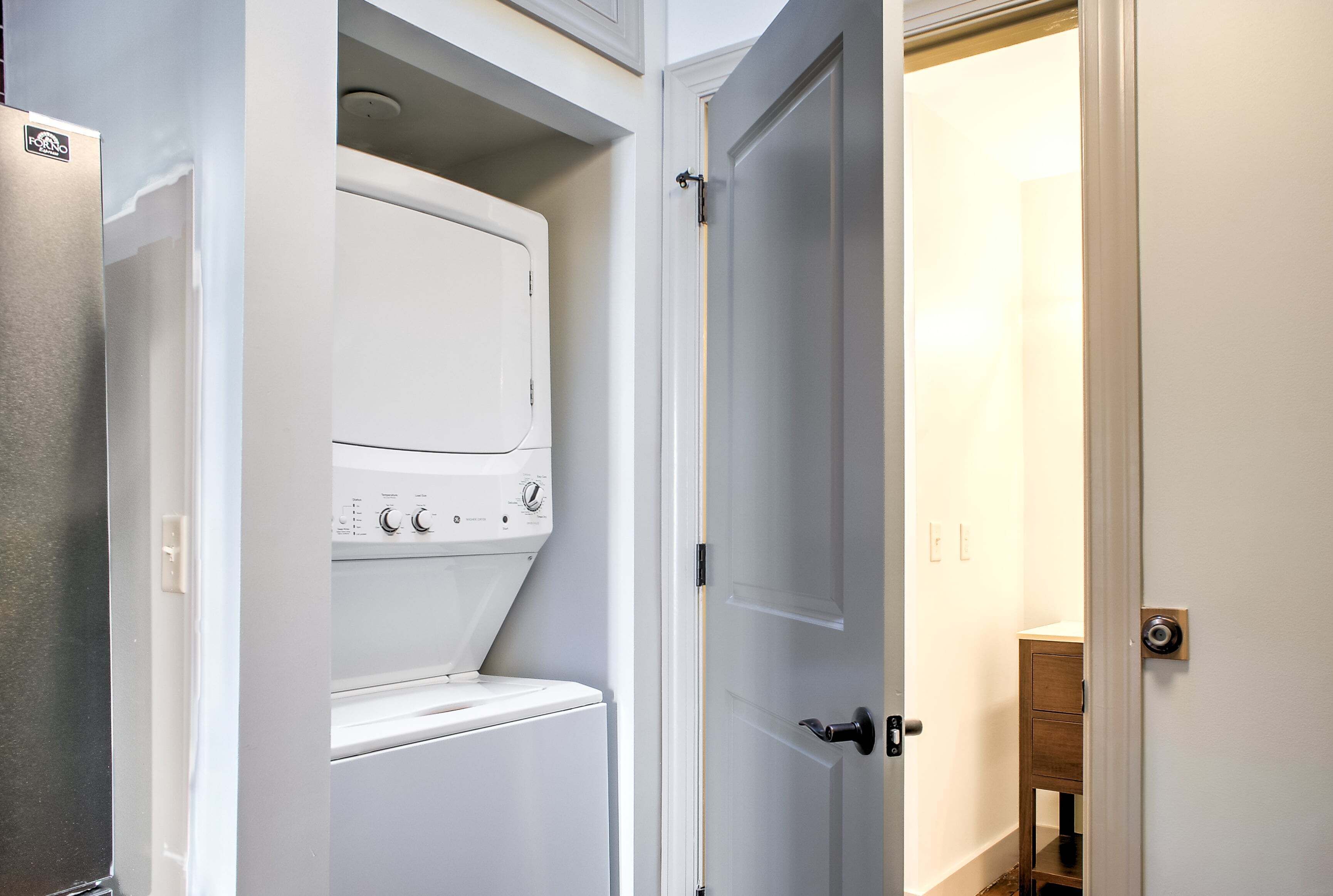 Ein Waschraum mit einer Frontlader-Waschmaschine und einem Trockner, einer Tür zu einem anderen Raum und einem kleinen Holzschrank.
