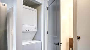 Ein Waschraum mit einer Frontlader-Waschmaschine und einem Trockner, einer Tür zu einem anderen Raum und einem kleinen Holzschrank.