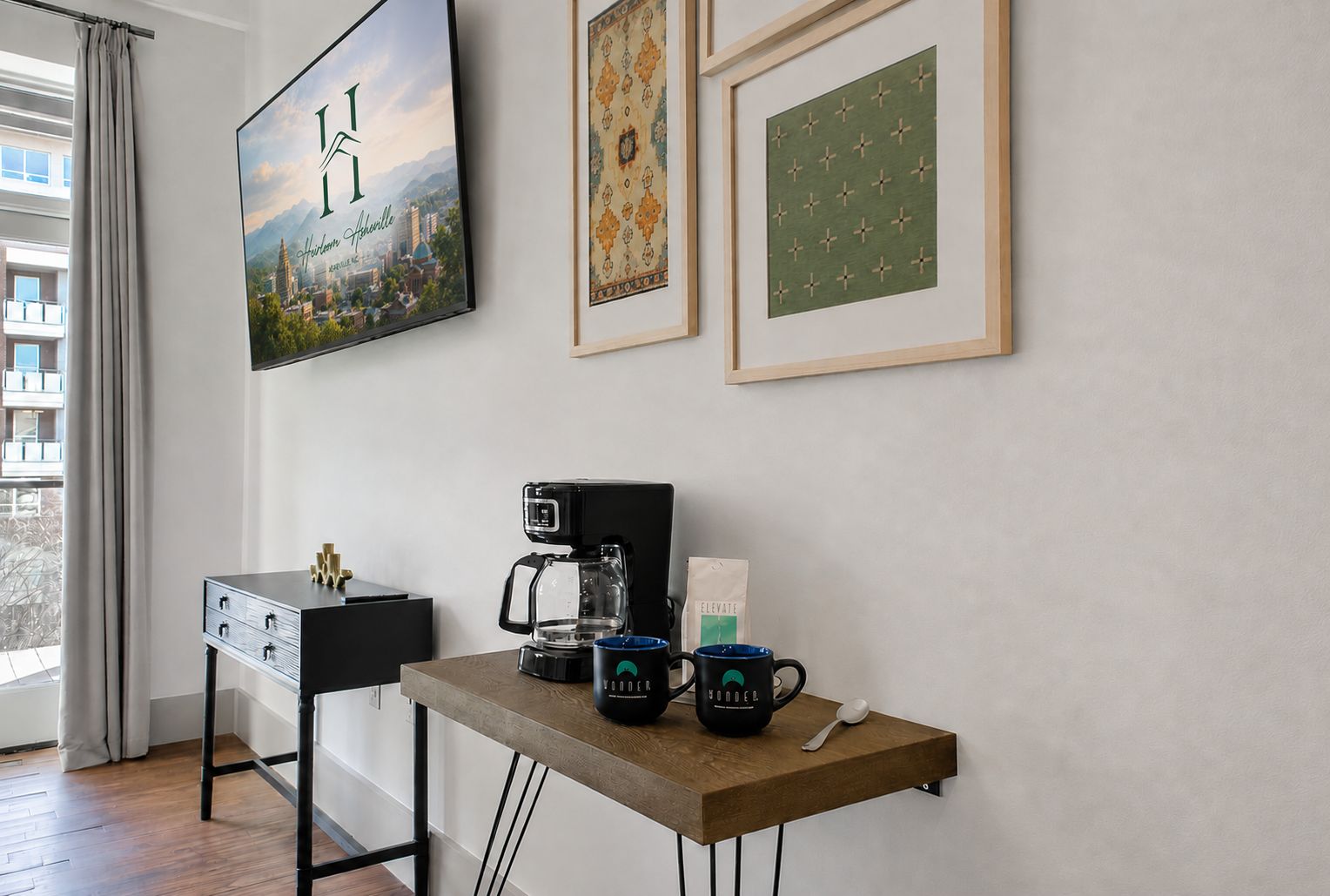 Una stanza con una scrivania, una macchina per il caffè, una confezione di caffè, due tazze e un cucchiaino. Alle pareti, si vedono quadri incorniciati.