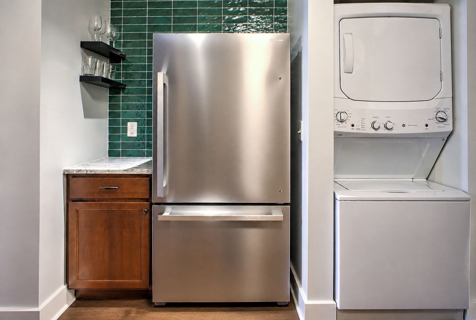 A compact kitchen with a stainless steel refrigerator, a built-in oven, and a washing machine.