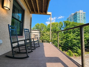 Ein Balkon mit zwei Schaukelstühlen, einer Holzpergola und Blick auf eine Skyline mit hohen Gebäuden.
