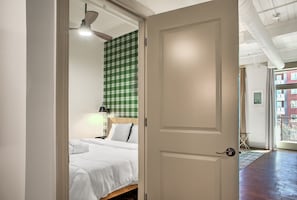 A bedroom with a bed, a green checkered wall, a ceiling fan, and a door leading to a balcony.