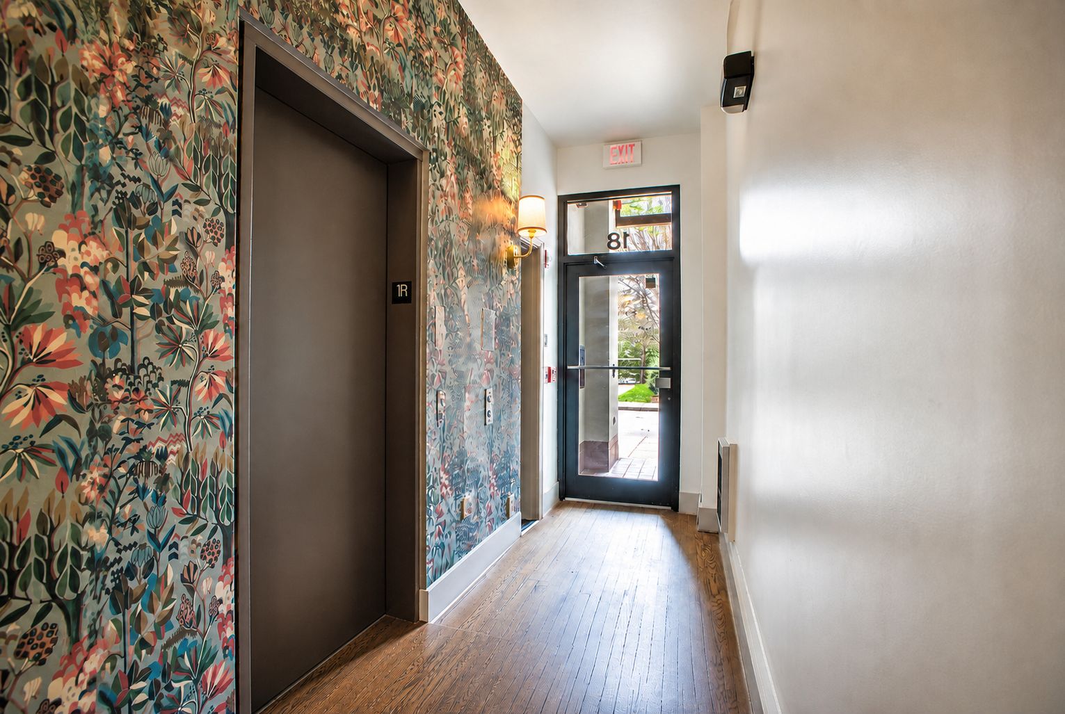 A hallway with a floral wallpaper, a door with a number sign, and a light fixture.