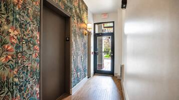 A hallway with a floral wallpaper, a door with a number sign, and a light fixture.