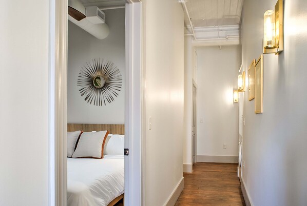 Ein Hotelgang mit einem Bett, einem an der Wand befestigten Spiegel und einer dekorativen Sonnenscheibeleuchte.