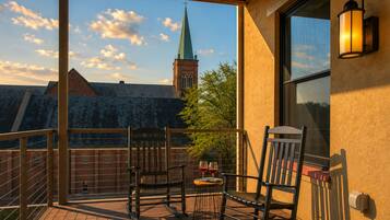 A balcony with two rocking chairs, a small table with wine glasses, and a view of a church steeple.
