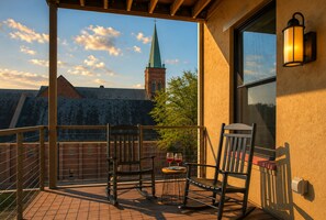 A balcony with two rocking chairs, a small table with wine glasses, and a view of a church steeple.