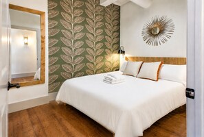 A hotel room with a bed, a mirror, a wall clock, and a patterned wallpaper.
