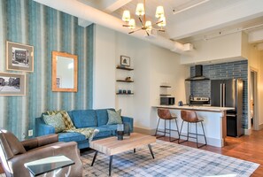 Ein Wohnzimmer mit Sofa, Couchtisch und Sesseln, eine Küche mit Kühlschrank und Mikrowelle sowie eine Essecke mit Hocker.