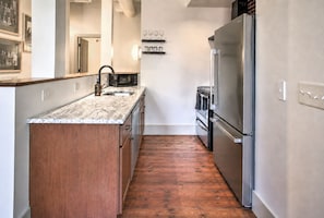 A narrow kitchen with a wooden floor, a marble countertop, and stainless steel appliances including a refrigerator and oven. - The Gatsby at Heirloom Asheville | Downtown Asheville Historic Condo with Two King Suites (Asheville)