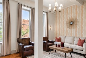 A room with a leather armchair, a sofa, a coffee table, and a patterned wall. - The Gatsby at Heirloom Asheville | Downtown Asheville Historic Condo with Two King Suites (Asheville)
