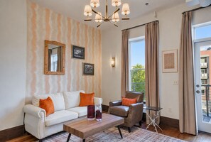 A living room with a sofa, armchair, coffee table, and a large window with curtains. - Downtown Asheville Condo with Private Deck | The Pisgah at Heirloom Asheville (Asheville)
