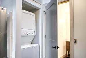 Ein Waschraum mit einer Frontlader-Waschmaschine und einem Trockner, einer Tür zu einem anderen Raum und einem kleinen Holzschrank.
