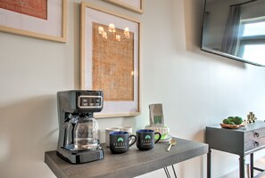 Une machine à café, deux tasses, un tableau encadré, un téléviseur et une petite plante sur une table.