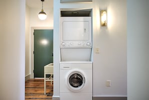 Un espace buanderie compact avec un lave-linge et un sèche-linge à chargement frontal, un plancher en bois et une porte verte en arrière-plan.
