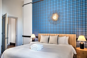 Ein Hotelzimmer mit einem Bett, zwei Nachttischen mit Lampen, einer Wanduhr und einer Tür.