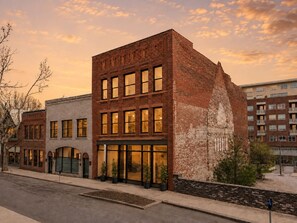 A multi-story building with a brick facade, large windows, and a landscaped area with potted plants. - Heirloom Asheville | 8 Private Luxury Condos in Downtown Asheville (Asheville)