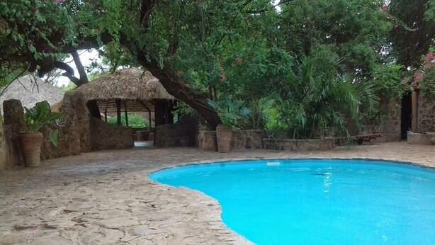 A pool area with stone flooring, a thatched-roof structure, and lush greenery. - Trackmark Hotel Lokichogio  (Lokichogio)