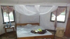 A single bed with a wooden frame and white bedding, a small bedside table, and a window with curtains. - Trackmark Hotel Lokichogio  (Lokichogio)