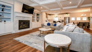 A spacious living room with a fireplace, a television mounted above it, and a dining area with a chandelier. - Modern Gated Retreat w/Rooftop Views, Med Ctr & Downtown (Houston)