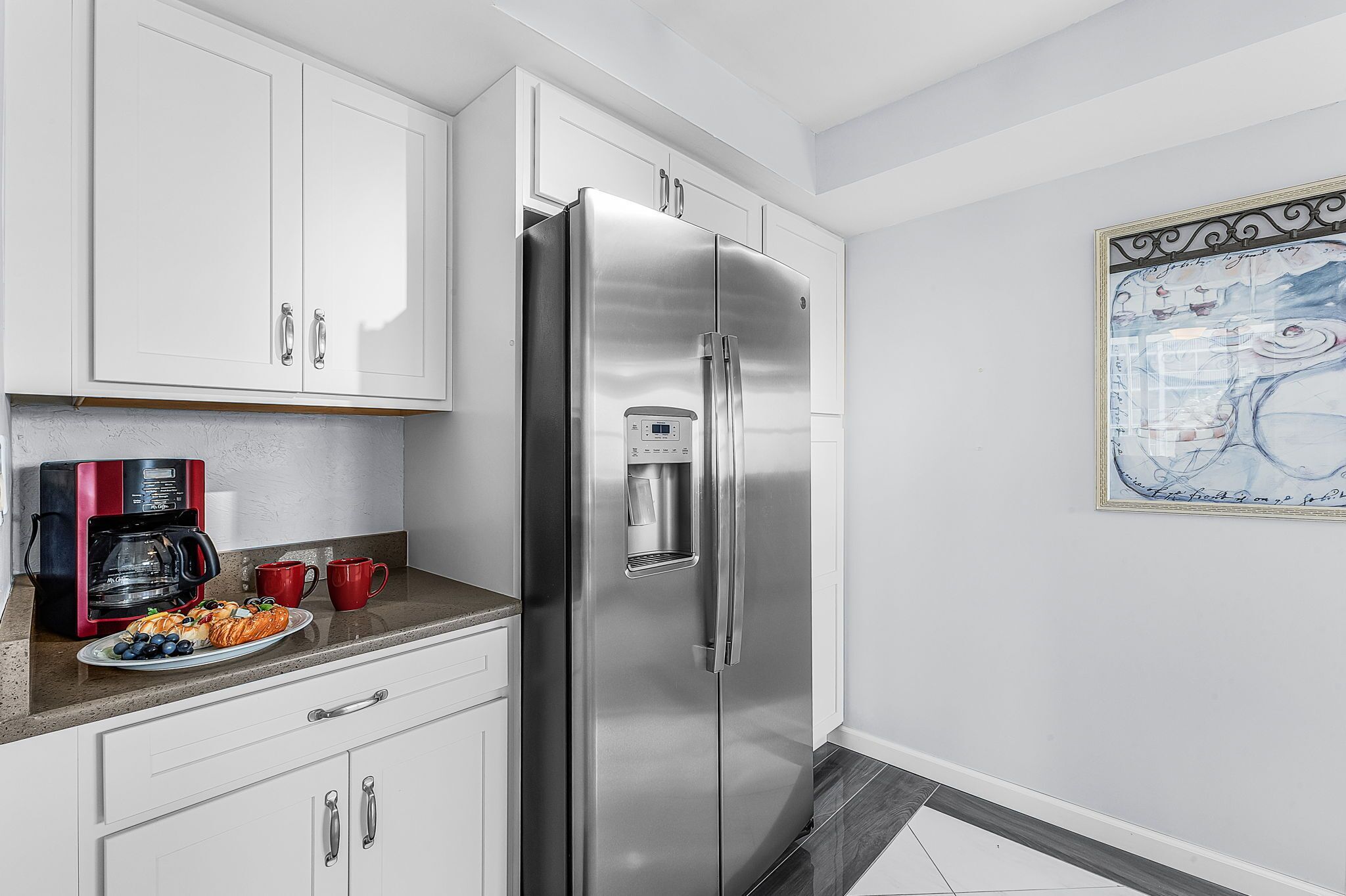 A kitchen with a stainless steel refrigerator, white cabinets, a coffee maker, and a plate of food.