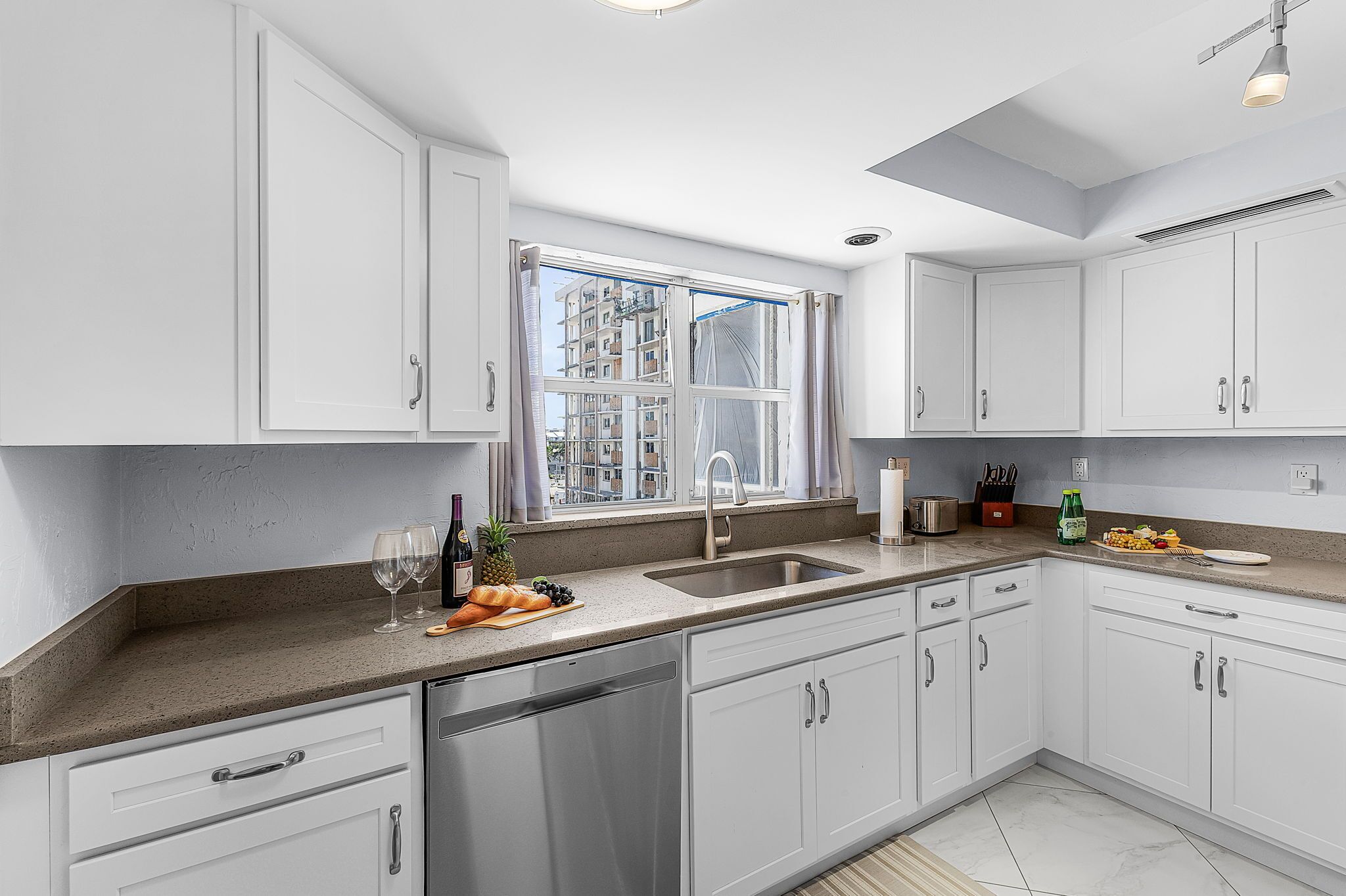 A modern kitchen with white cabinets, a stainless steel sink, and a window with a view of buildings.