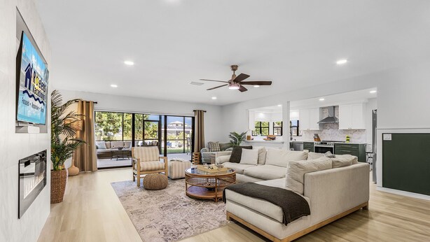 A spacious living area with a sofa, armchairs, and a coffee table. A ceiling fan and a TV are mounted on the wall. - Operation Relaxation heated Pool & Spa, Bicycles - At Ease - Roelens (Cape Coral)