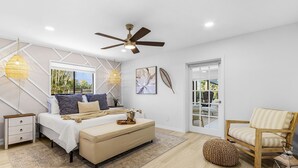 A modern bedroom with a bed, bedside tables, a ceiling fan, and a view of the outdoors. - Operation Relaxation heated Pool & Spa, Bicycles - At Ease - Roelens (Cape Coral)