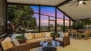A spacious outdoor seating area with wicker furniture and a glass table, overlooking a lush garden and a sunset view. - Operation Relaxation heated Pool & Spa, Bicycles - At Ease - Roelens (Cape Coral)