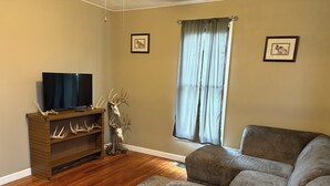 Una sala de estar con una unidad de entretenimiento de madera, un sofá gris, un ventanal con cortinas y dos cuadros enmarcados en las paredes.